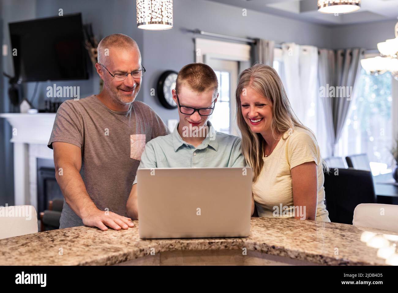Hombre joven usando una computadora portátil en casa con sus padres mirando; Edmonton, Alberta, Canadá Foto de stock