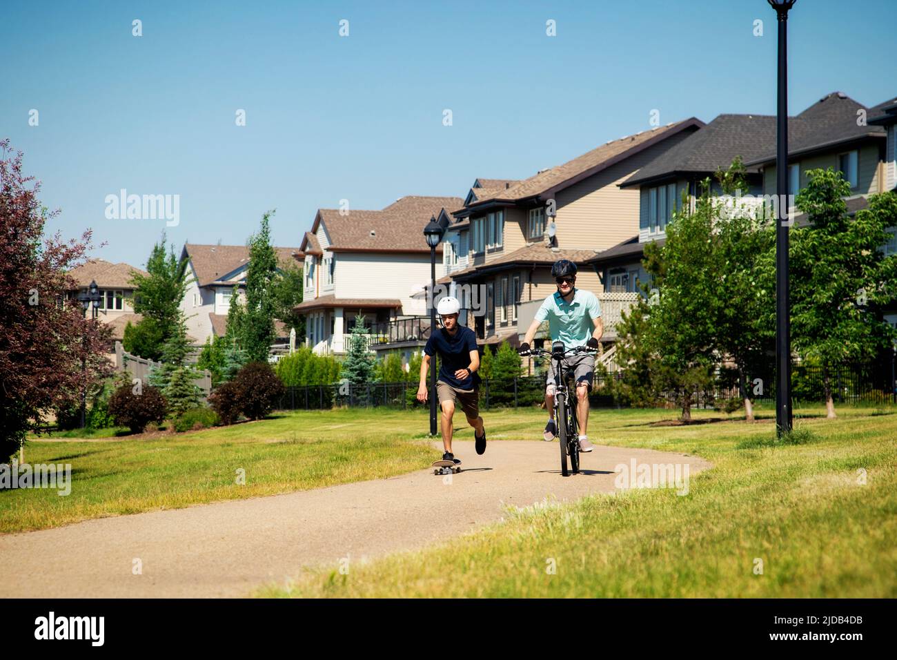 Hermanos que pasan tiempo juntos en el vecindario, uno en bicicleta y otro en monopatín; Edmonton, Alberta, Canadá Foto de stock