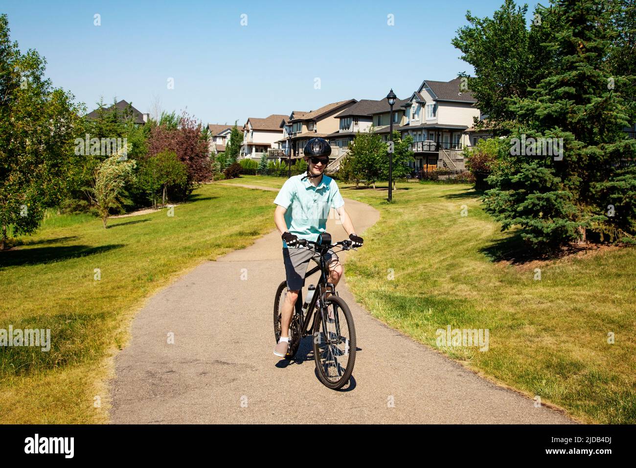 Joven montando su bicicleta por un camino en un parque residencial; Edmonton, Alberta, Canadá Foto de stock