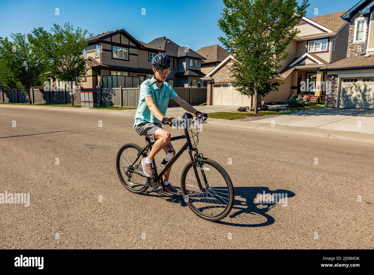 Joven montando su bicicleta por una calle residencial; Edmonton, Alberta, Canadá Foto de stock