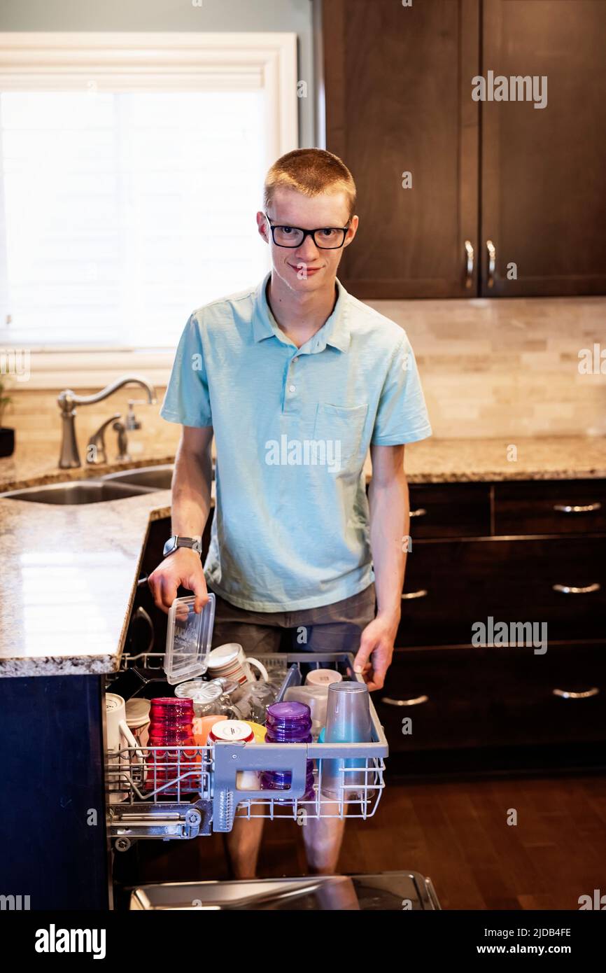 Joven descarga el lavavajillas en casa; Edmonton, Alberta, Canadá Foto de stock
