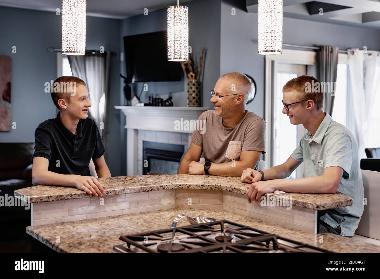 Padre y dos hijos se sientan en la isla de la cocina en casa hablando juntos; Edmonton, Alberta, Canadá Foto de stock