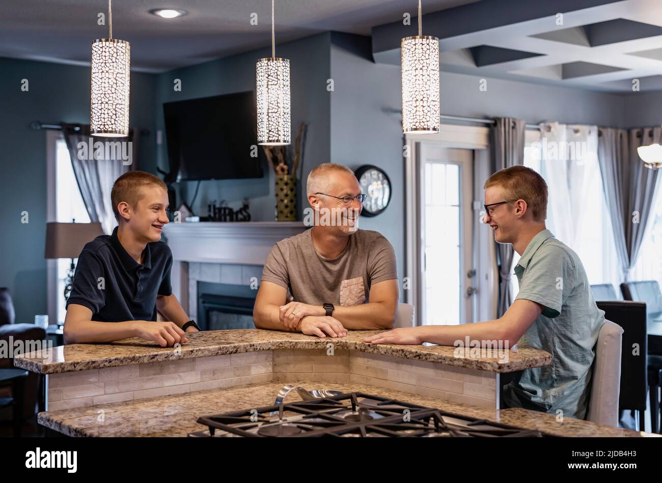 Padre y dos hijos se sientan en la isla de la cocina en casa hablando juntos; Edmonton, Alberta, Canadá Foto de stock