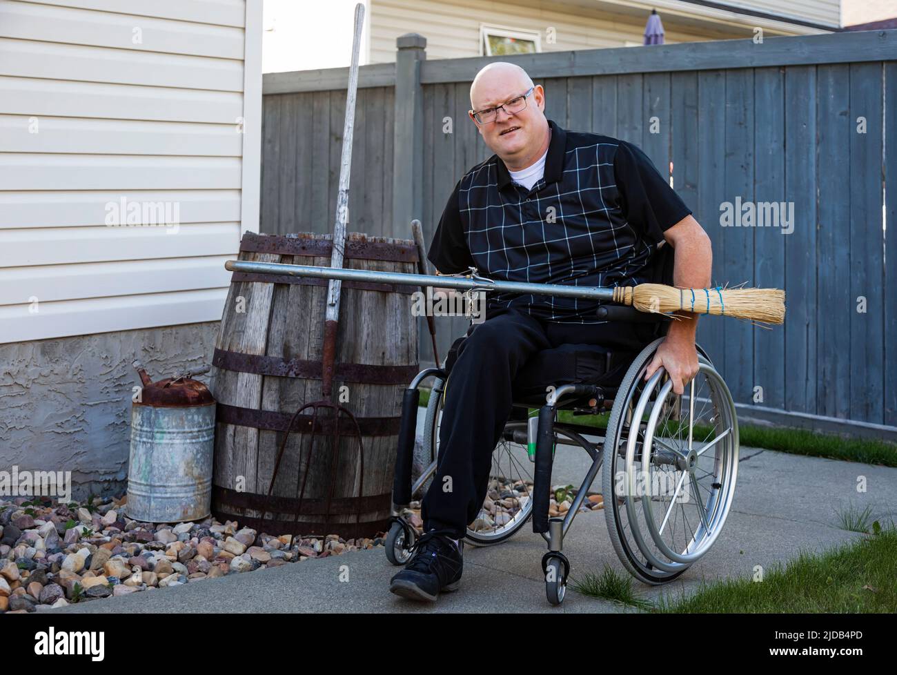 Hombre con amputaciones de doble extremidad haciendo trabajo de patio en su patio trasero con una escoba; St. Albert, Alberta, Canadá Foto de stock