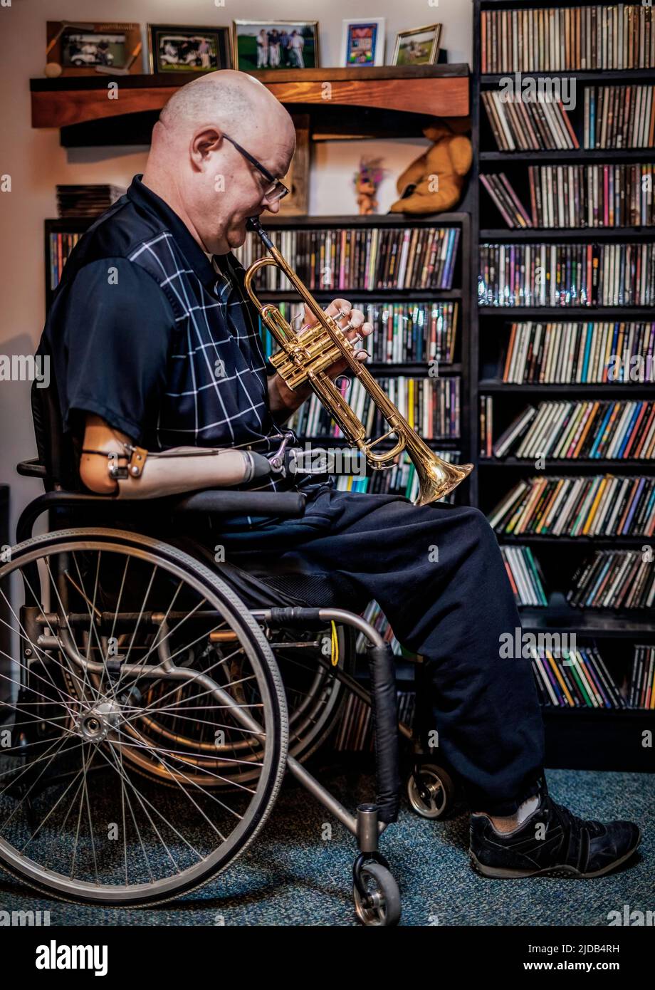 Hombre con amputaciones de doble extremidad tocando la trompeta en casa; St. Albert, Alberta, Canadá Foto de stock