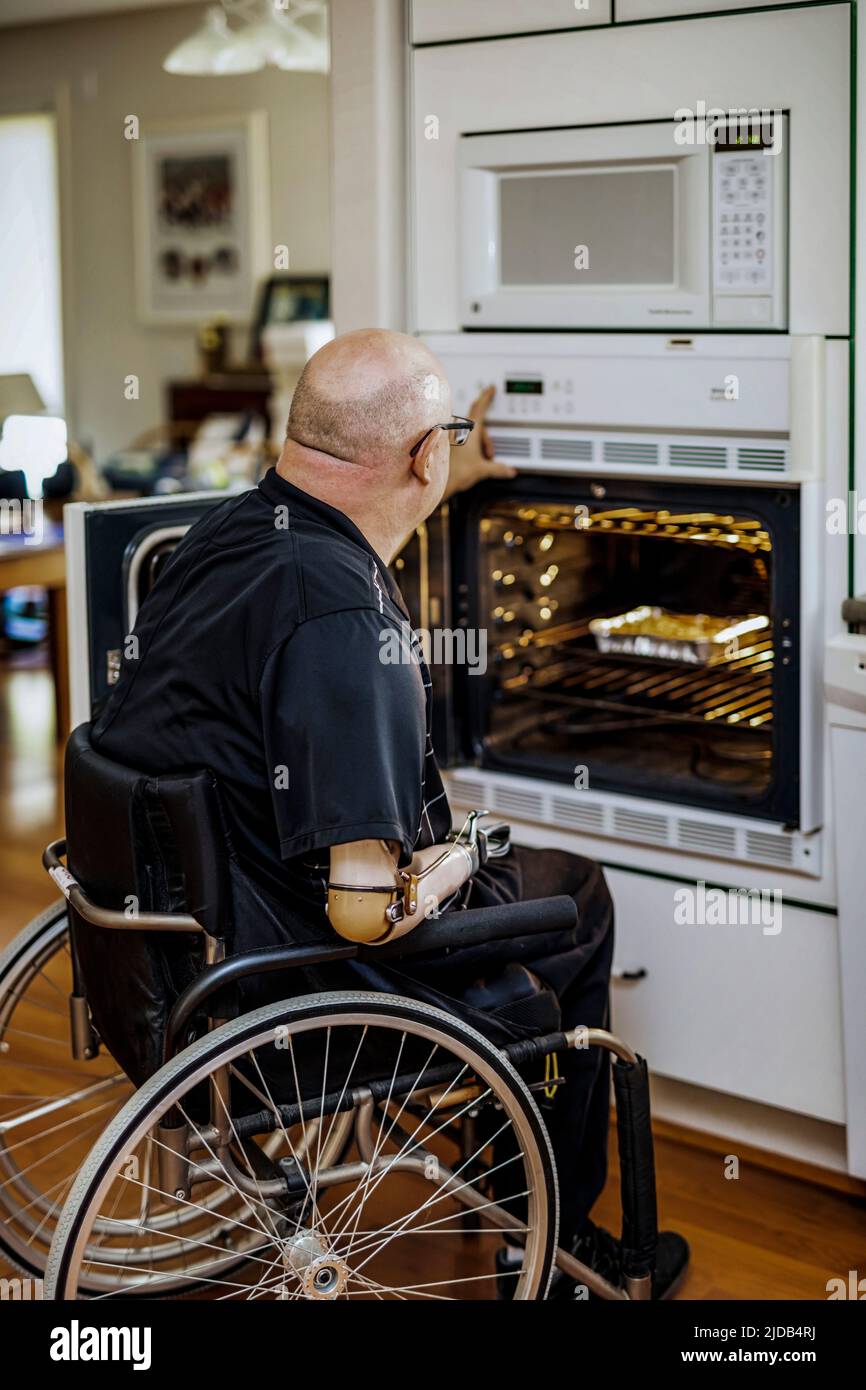 Hombre con amputaciones de doble extremidad usando el horno en la cocina en casa; St. Albert, Alberta, Canadá Foto de stock