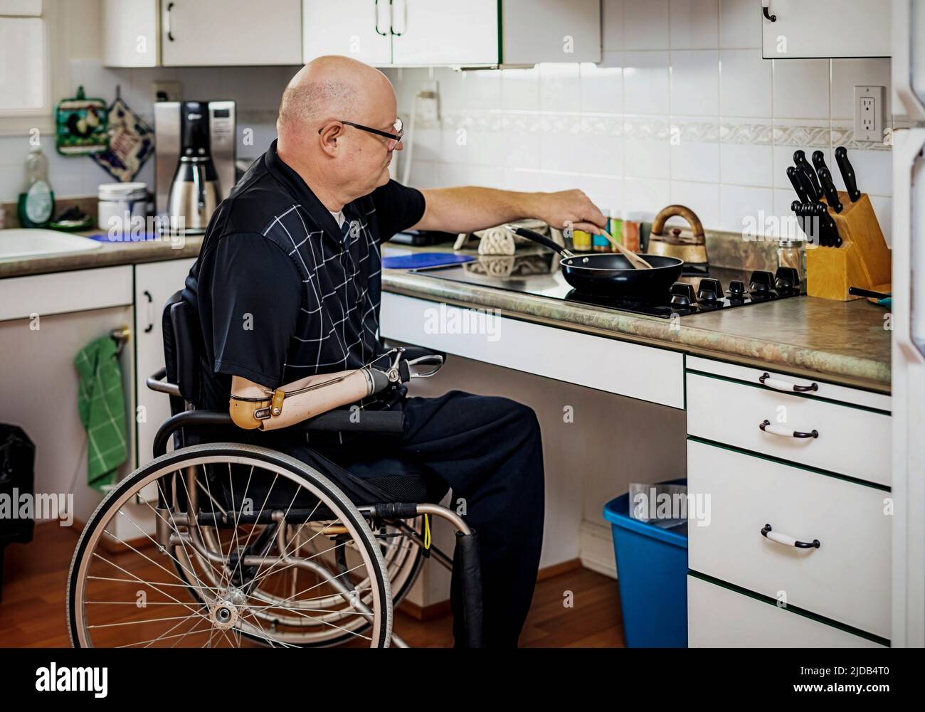 Hombre con amputaciones de doble extremidad cocinando en la estufa en la cocina en casa; St. Albert, Alberta, Canadá Foto de stock