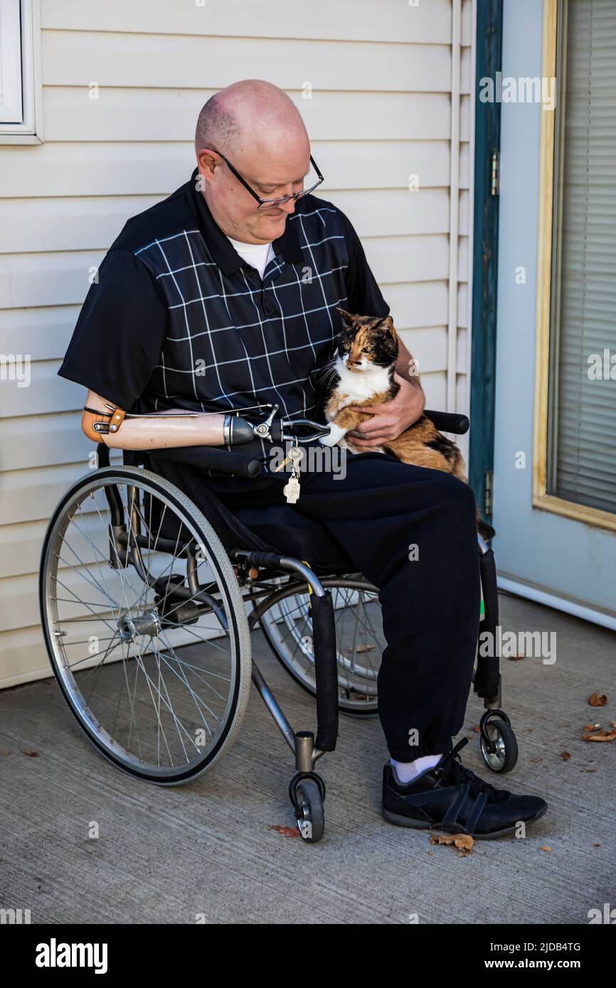 Hombre con amputaciones de doble extremidad sentado fuera de su casa con su gato mascota en su regazo; St. Albert, Alberta, Canadá Foto de stock