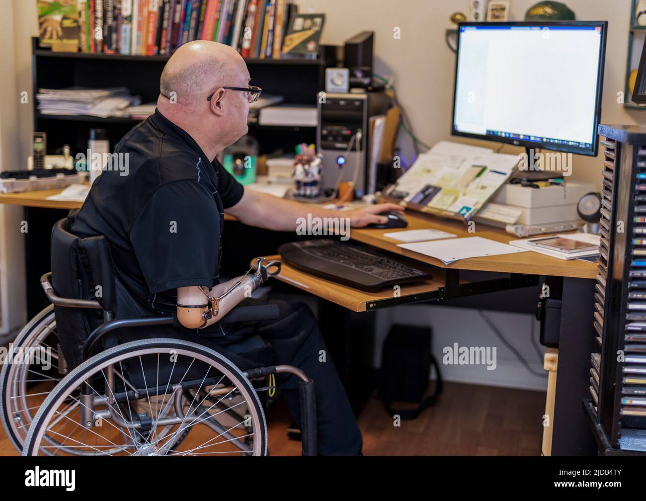 Hombre con amputaciones de doble extremidad trabajando remotamente desde casa en una computadora; St. Albert, Alberta, Canadá Foto de stock