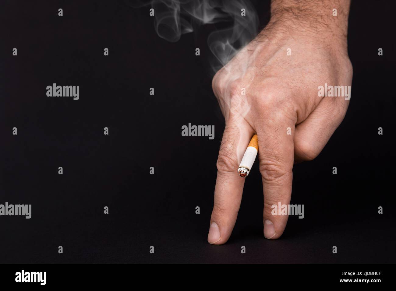 Impotencia en los hombres. Cigarrillo en mano con humo aislado sobre fondo negro, cerca. Daño de fumar para los hombres. Disfunción eréctil, impotencia en los hombres causada por fumar. Cigarrillo fumado en los dedos Foto de stock