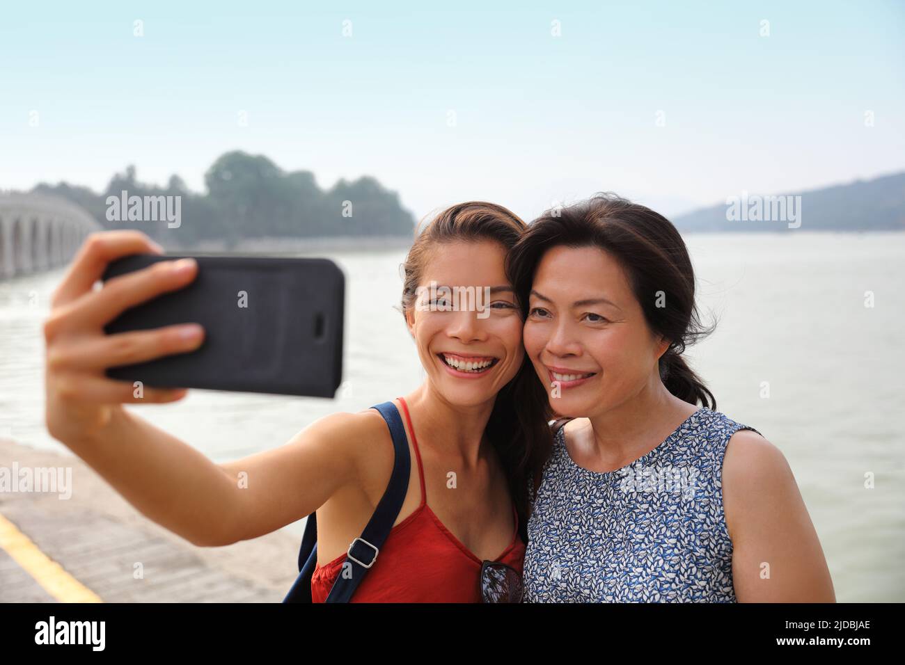 Madre hija adulta viajando juntos en Asia tomando foto selfie con el teléfono móvil. Sonriente familia asiática fuera Foto de stock