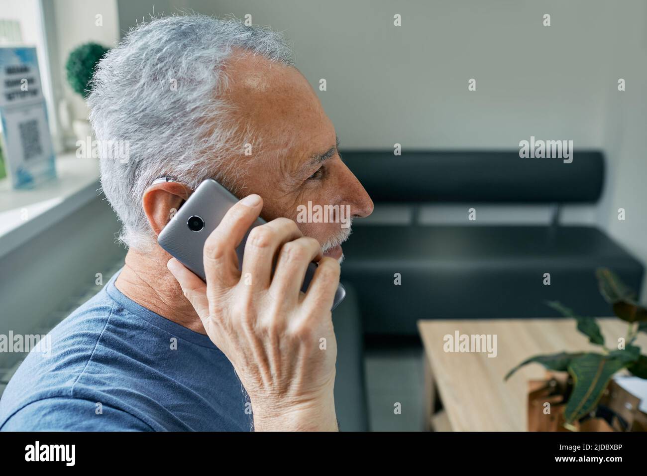 Uso de los audífonos con un smartphone . El hombre mayor con audífono detrás del oído tiene una vida completa y puede oír al interlocutor en el teléfono Foto de stock