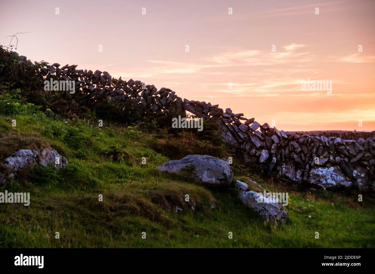 Las paredes de piedra se siluetaron contra una puesta de sol de finales de verano en la isla Aran de Inishmore en la bahía de Galway, Irlanda. Foto de stock