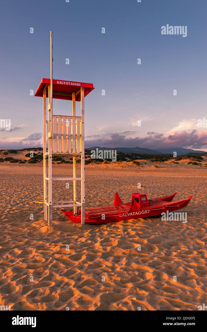 Salvataggio socorrista torre y barco salvavidas en la playa de arena de Piscinas en la luz dorada al atardecer, Costa Verde, Cerdeña, Italia Foto de stock