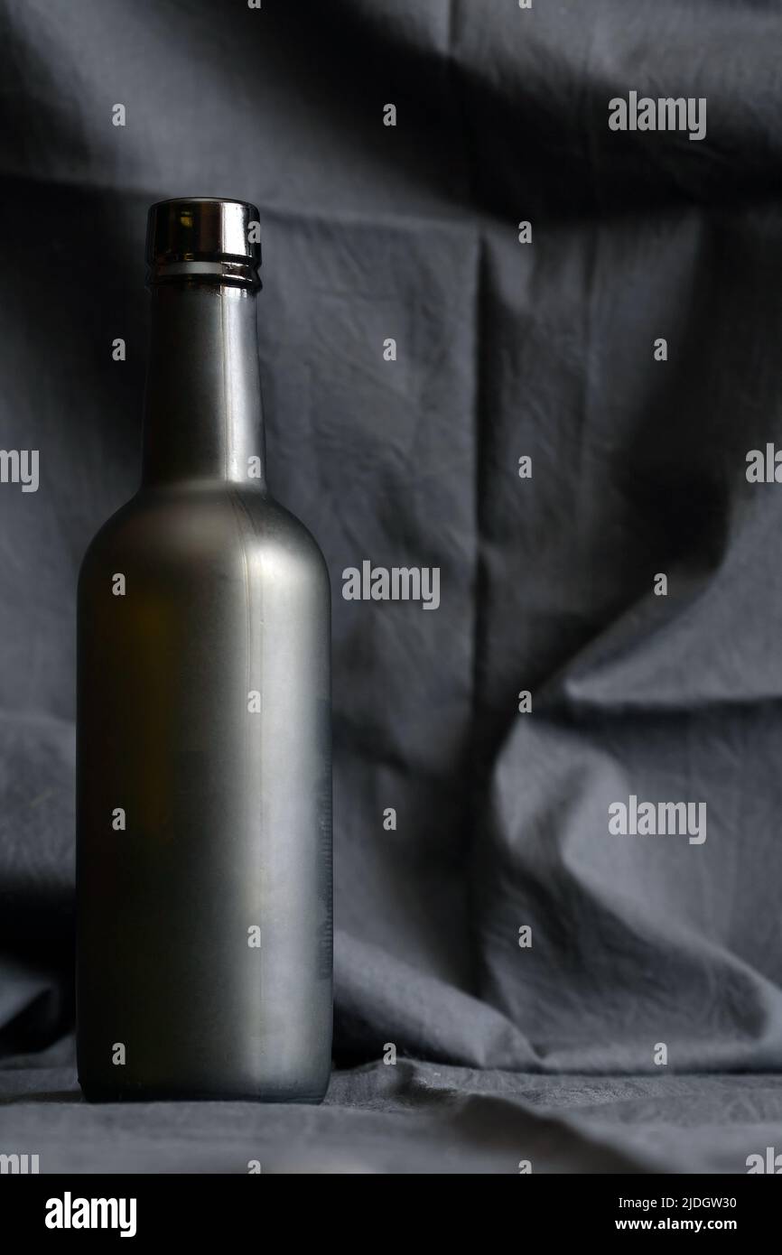 Una botella negra de cristal contra un bonito fondo textil oscuro Foto de stock