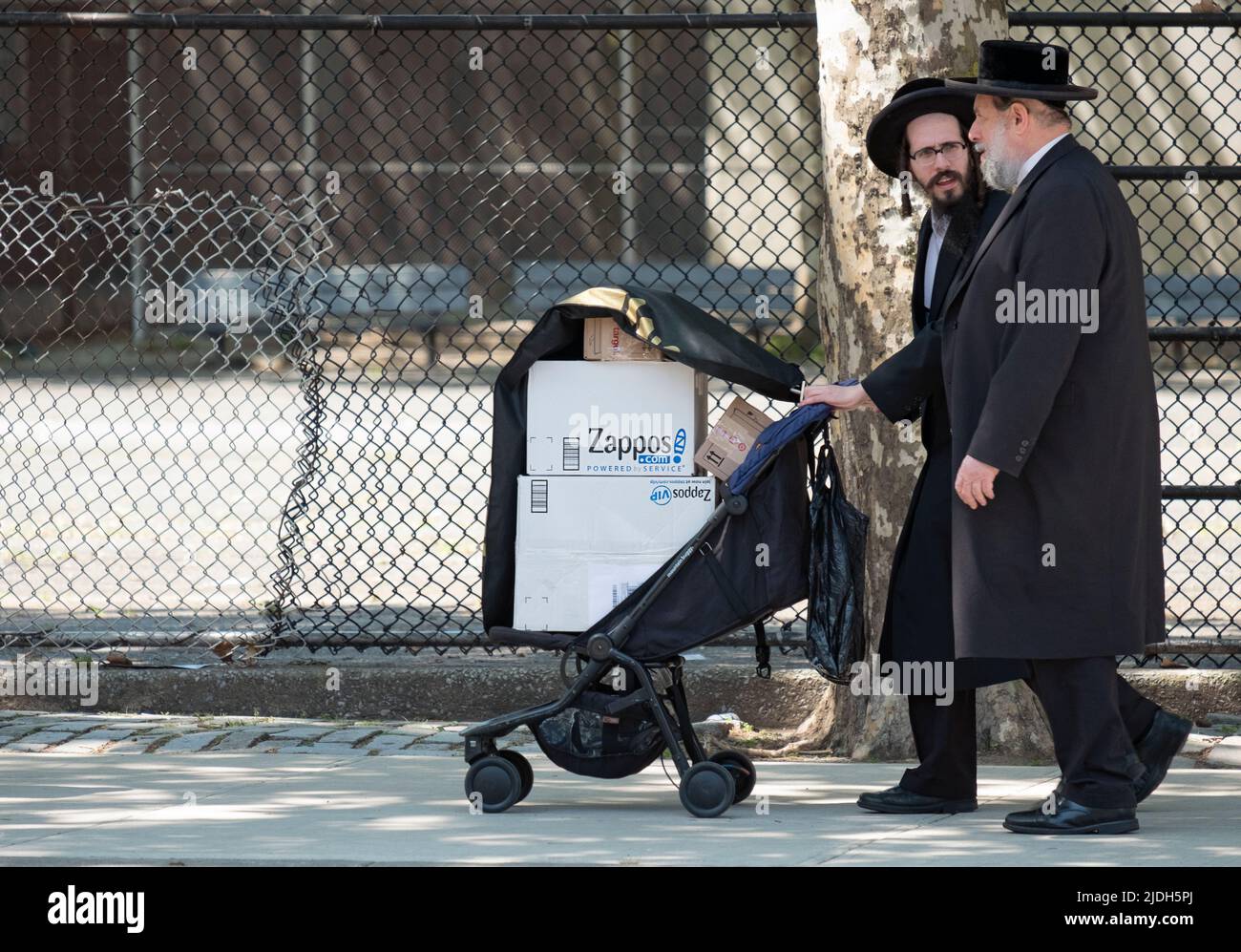 2 Hombres judíos Hasídicos, posiblemente familia, caminan por la avenida Lee usando un cochecito para llevar cajas de zapatos Zappos. En Williamsburg, Brooklyn, Nueva York. Foto de stock