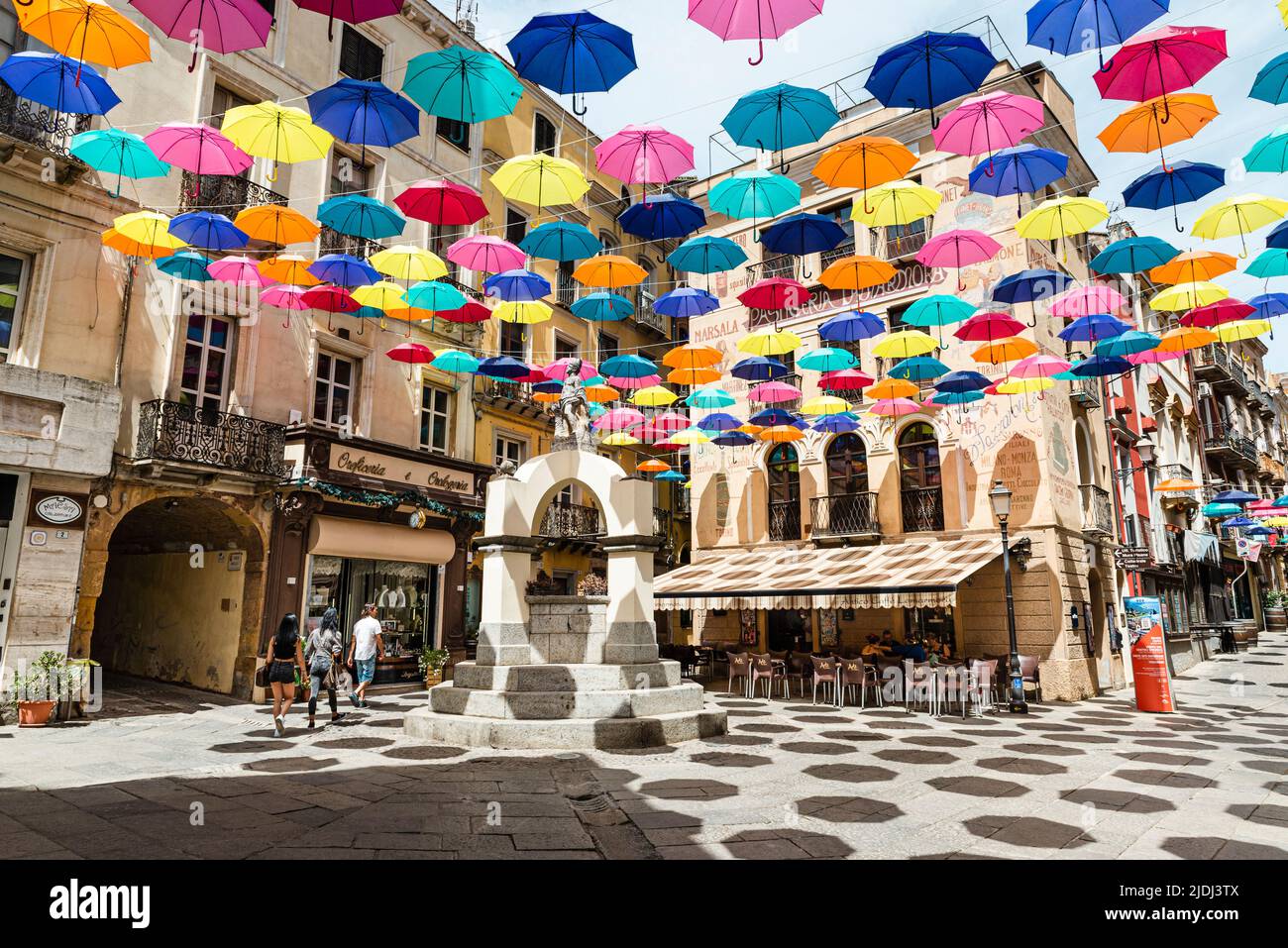 Las coloridas sombrillas protegen a los transeúntes en la Piazza Lamarmora, rodeada de casas históricas en el casco antiguo de Iglesias, en el suroeste de Cerdeña, Italia Foto de stock