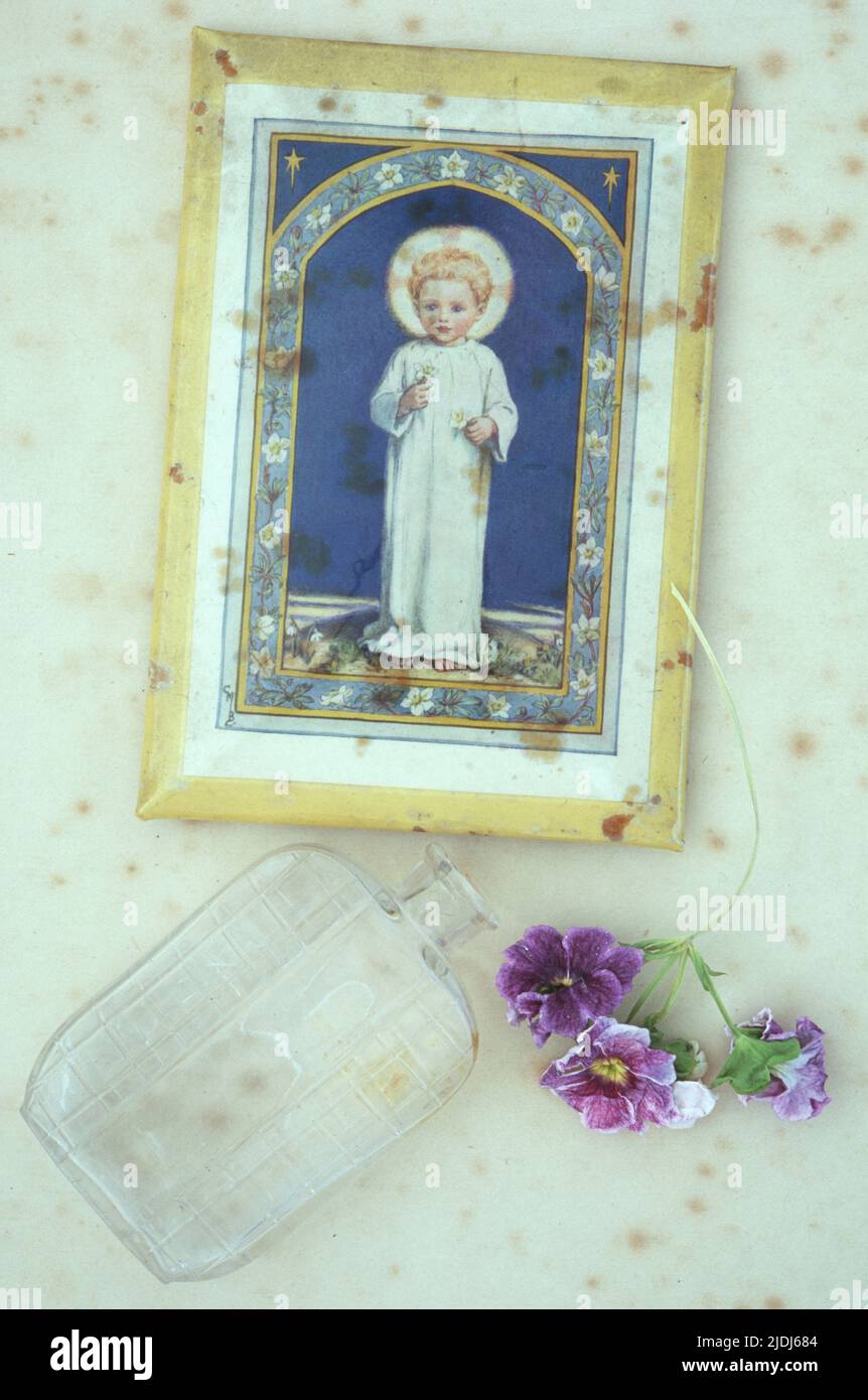 Estampado vintage de niño angelical con halo acostado sobre papel antiguo con una botella de perfume antigua y flores de Pelargonio de malva seca Foto de stock