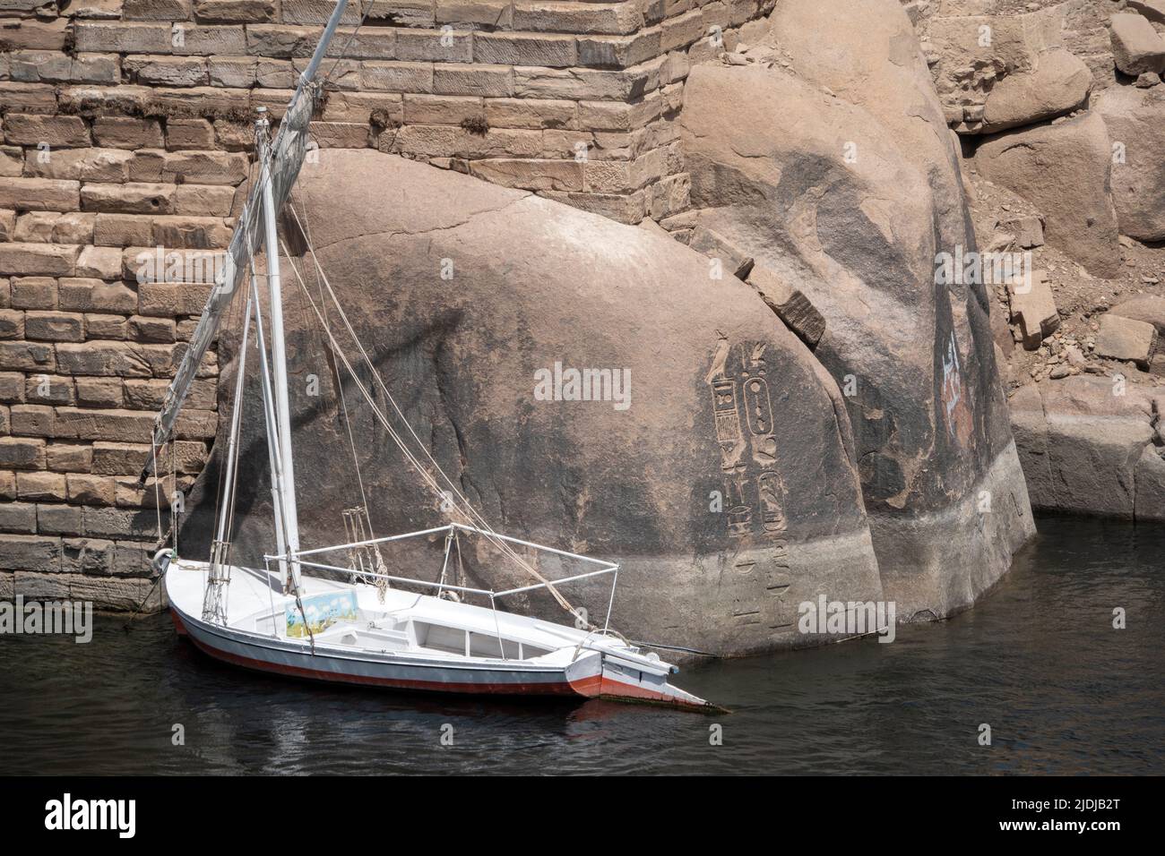 Felucca amarrada en Asuán frente a las rocas de granito con inscripciones faraónicas, Egipto Foto de stock