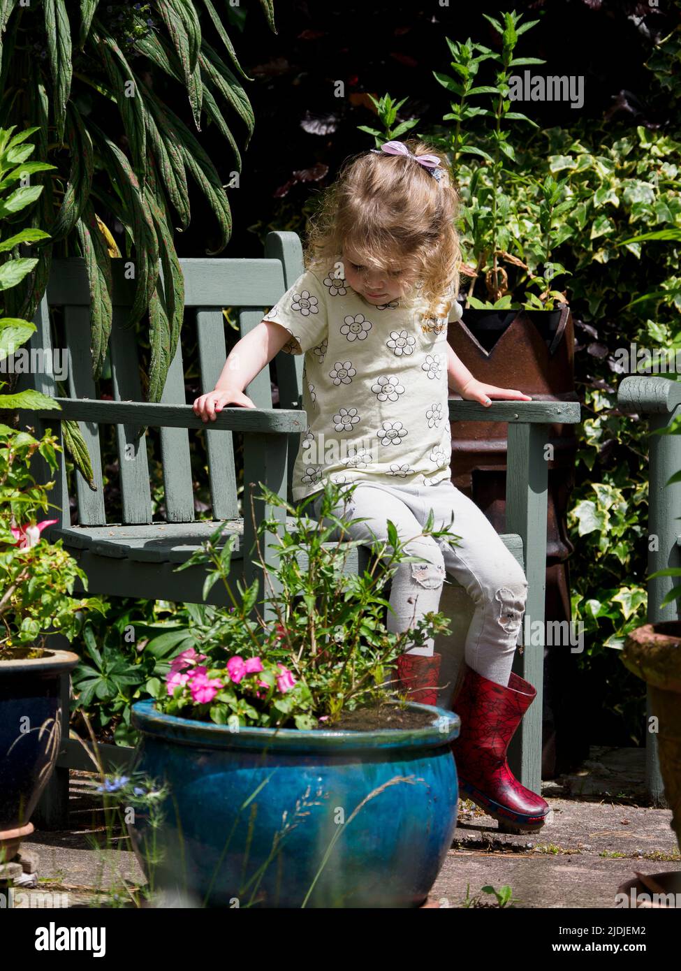 Un niño pequeño se sentó en una silla en el jardín, Reino Unido Foto de stock