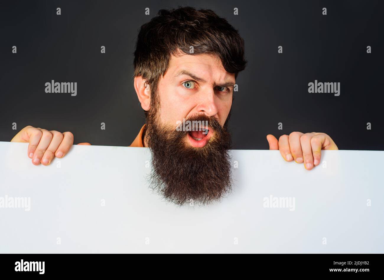 Hombre barbudo confundido con banner publicitario. Guapo muestra un tablero vacío con espacio para texto Foto de stock