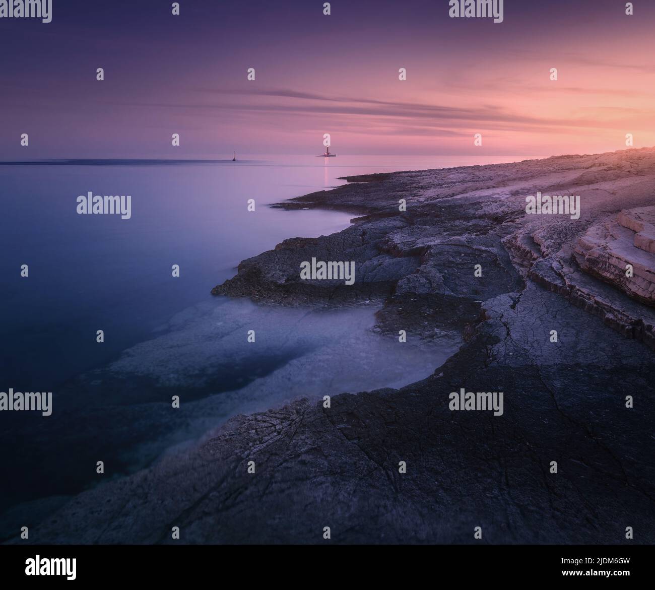 La costa rocosa del mar y el faro a la colorida puesta de sol en verano Foto de stock