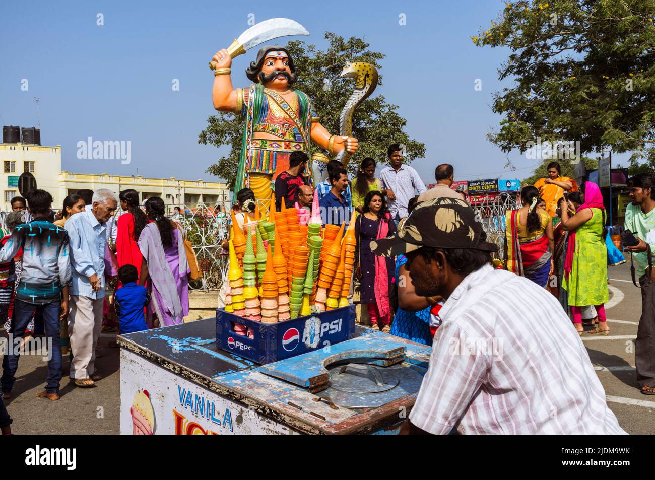 Chamundi Hill, Mysore, Karnataka, India : Un vendedor de helados empuja su carro por una colorida estatua fuera del Templo Sri Chamundeswari en Chamundi Foto de stock