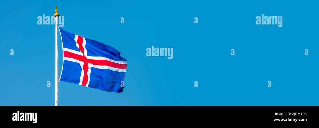 Bandera islandesa en un polo flotando en el viento sobre fondo azul cielo, web banner panorámico Foto de stock