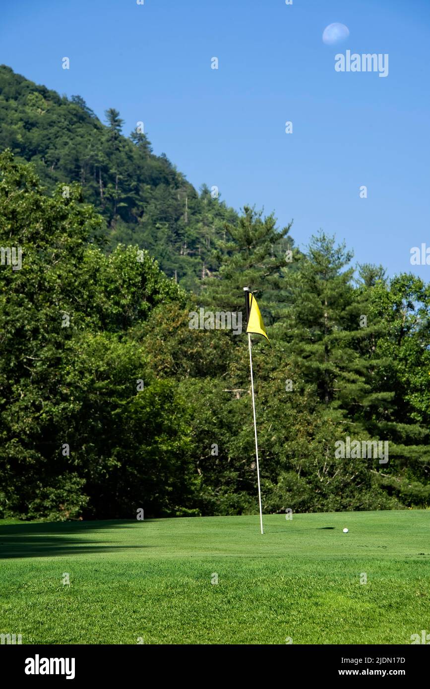 Bandera y pelota de golf sentarse en el verde, con una luna suave en el cielo. Foto de stock