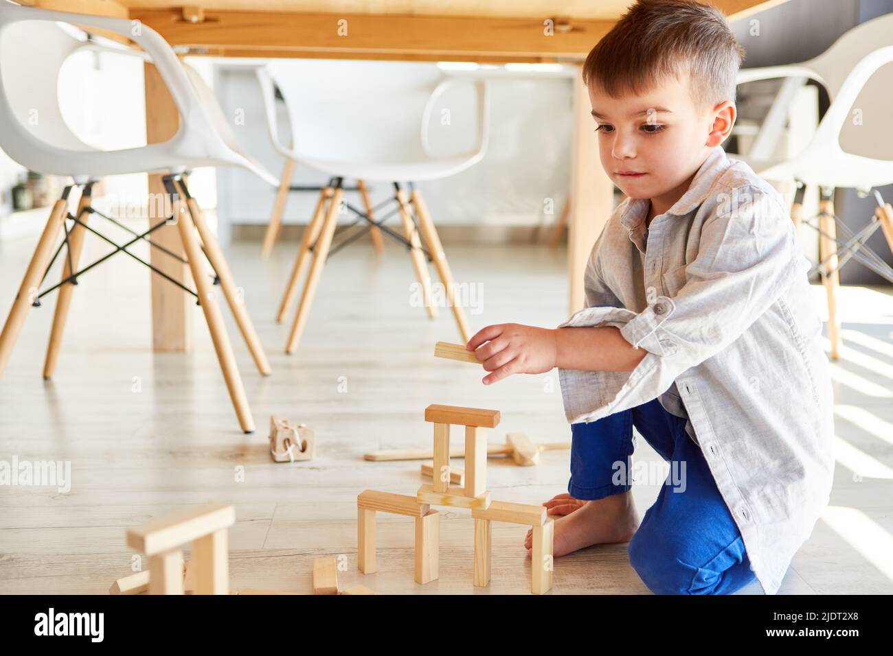 El niño pequeño se concentra en apilar bloques de madera para desarrollar habilidades motoras finas Foto de stock