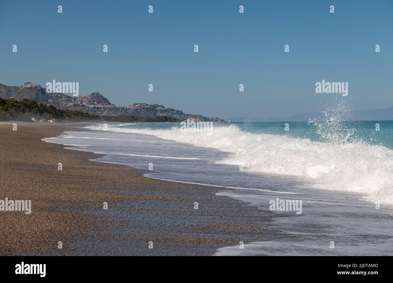 Rompiendo olas en la hermosa playa de Fondachello, Sicilia, Italia. Las populares ciudades de Taormina y Giardini Naxos se encuentran en la distancia Foto de stock