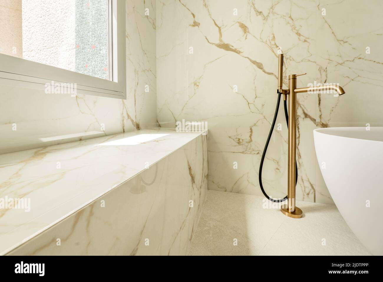 Detalle de un baño con paredes de mármol, un banco continuo hecho del mismo  material, grifos de latón y una bañera blanca separada Fotografía de stock  - Alamy