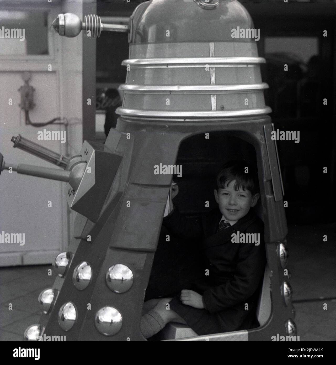 1967, histórico, un joven sentado en un Dalek, Inglaterra, Reino Unido. Una raza extraterrestre ficticia de mutantes o robots, los Daleks aparecieron por primera vez en el programa de televisión de ciencia ficción Briitsh Doctor Who en 1963. Creado por Terry Nation, los Daleks pronto se convirtieron en el personaje más popular de la BBC. Los alienígenas con aspecto distintivo de las conchas o las máquinas de viaje fueron diseñados por Raymond Cusick, que como empleado asalariado de la BBC en ese momento, no recibió ninguno de los ingresos generados por la mercancía de los Daleks, a diferencia de Nation que lo hizo, como fue un escritor independiente de guiones. Foto de stock