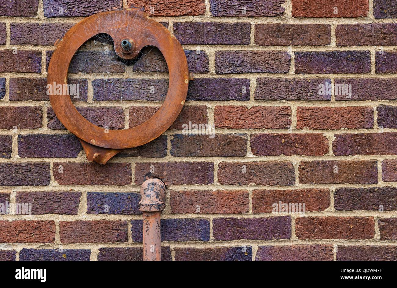 Banckground foto de una pared exterior de ladrillo con una tubería de hierro entrando en ella y una pieza de hierro en forma redonda oxidada adherida a ella. Foto de stock