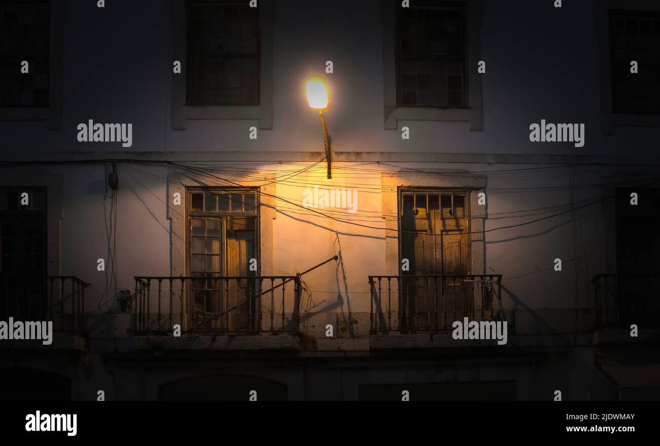 Una linterna brilla por la noche sobre dos pequeños balcones en un edificio antiguo. Fondo abstracto. Lisboa, Portugal. Foto de stock