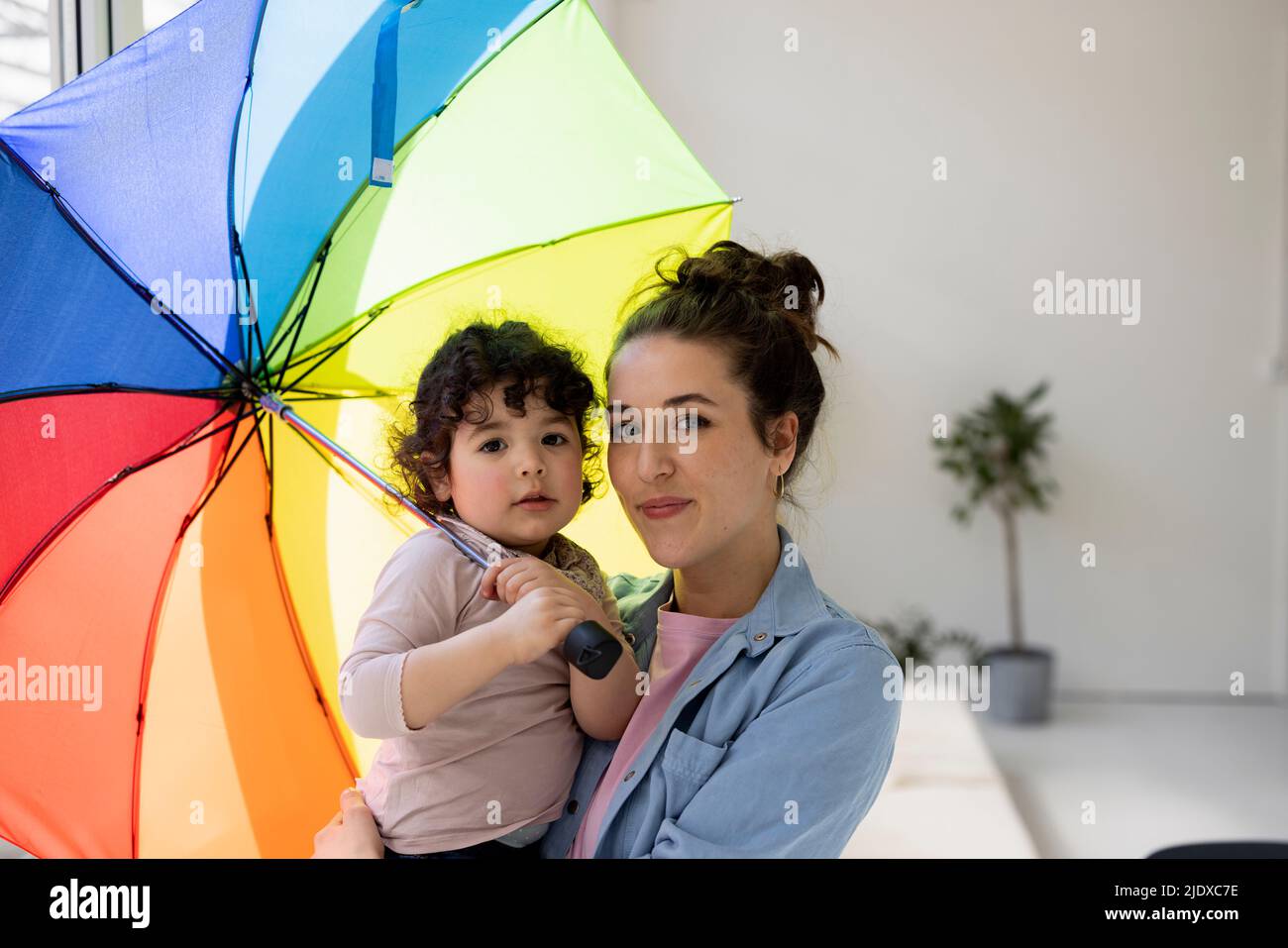 Madre e hija de pie en casa sosteniendo un paraguas Foto de stock