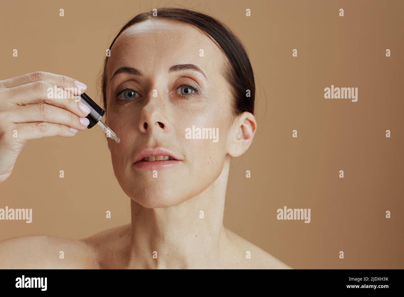moderna mujer de 40 años con elixir cosmético aislado en beige. Foto de stock