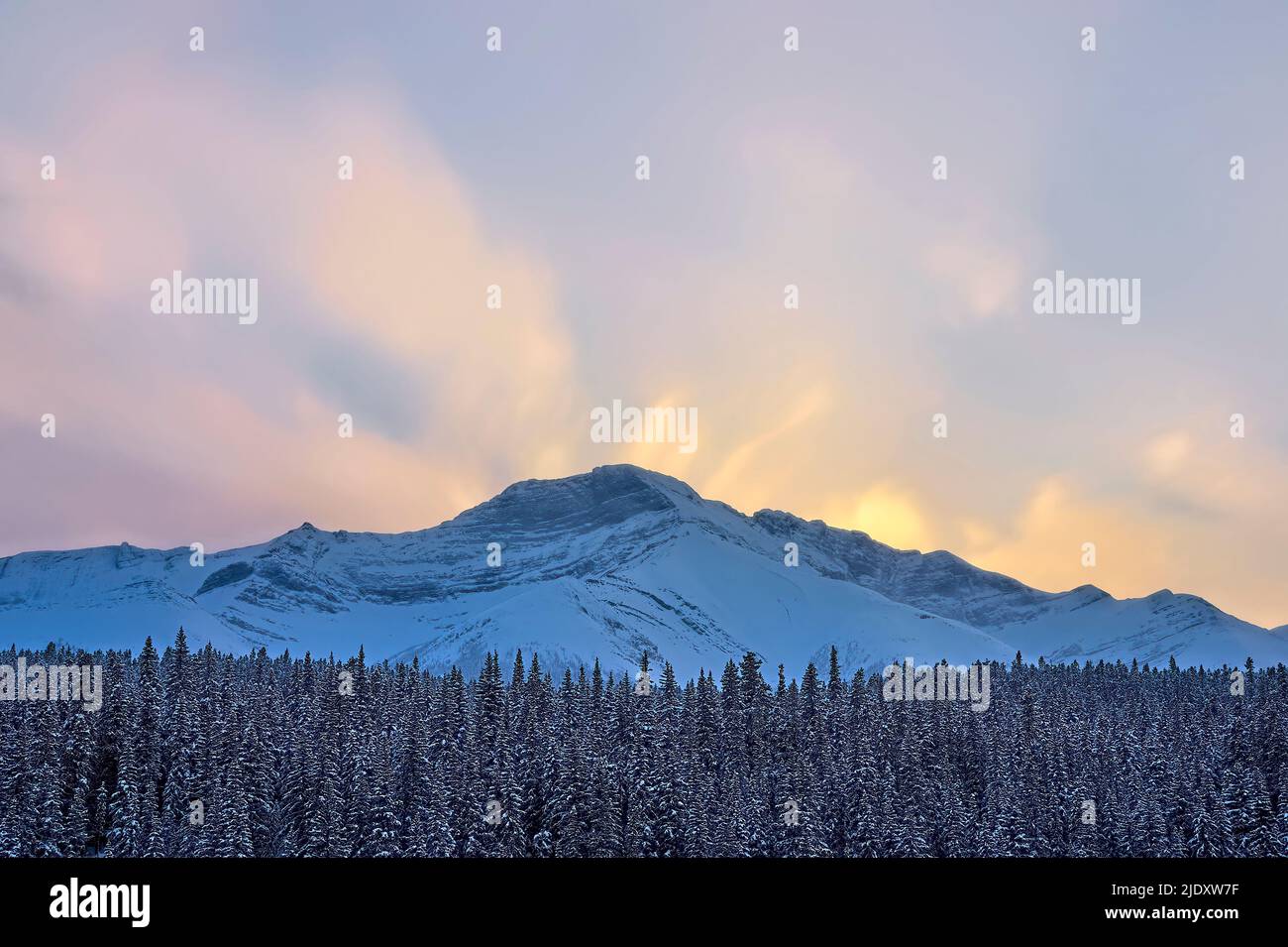 Un hermoso cielo de invierno sobre una montaña rocosa nevada en el oeste de Alberta, Canadá Foto de stock