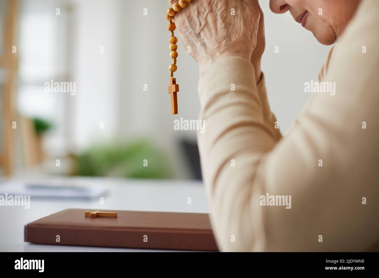 Mujer cristiana mayor orando a Dios y sosteniendo cuentas de rosario sobre la Santa Biblia Foto de stock