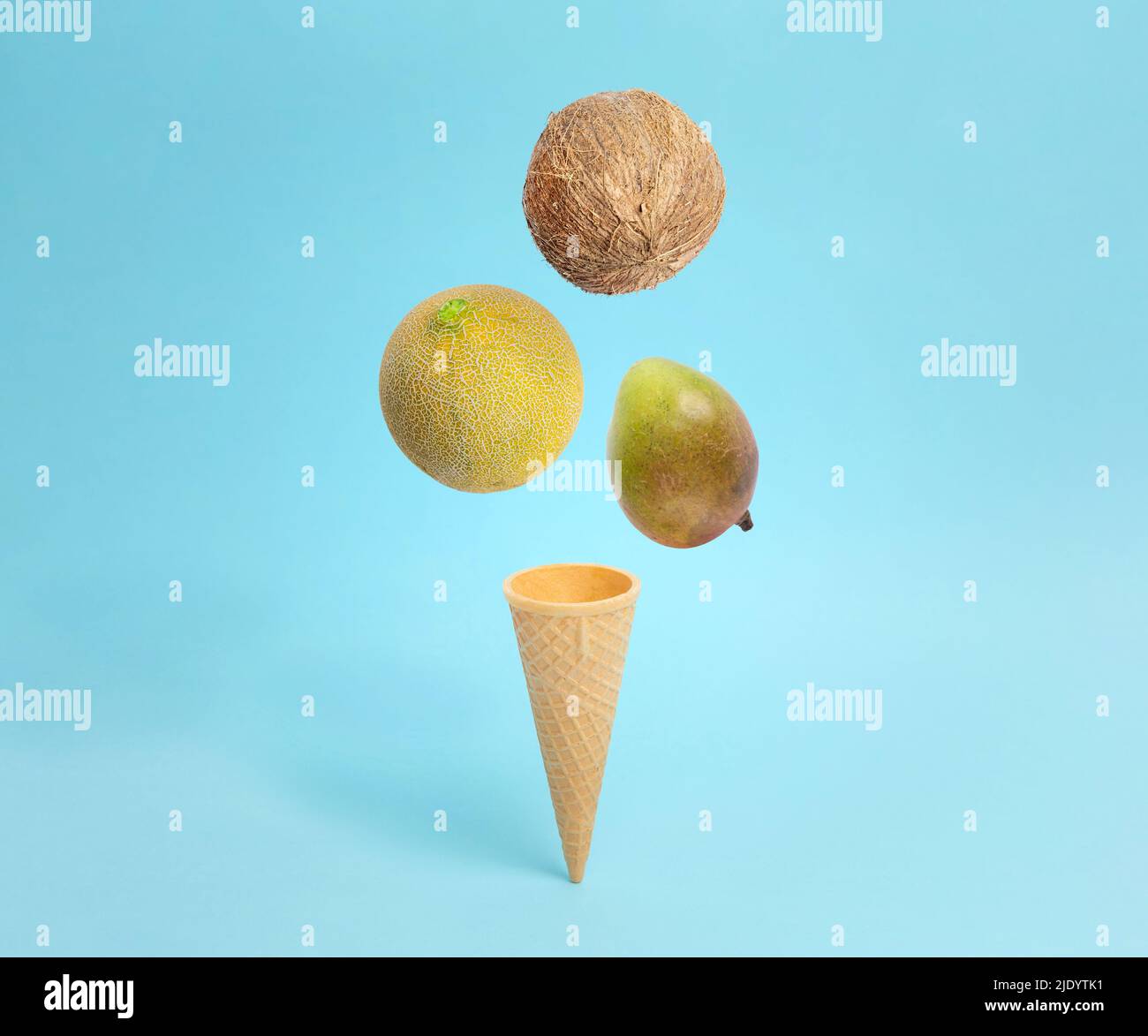 Helado de cono con coco, melón y caída de mango. Composición conceptual creativa en azul pastel Foto de stock
