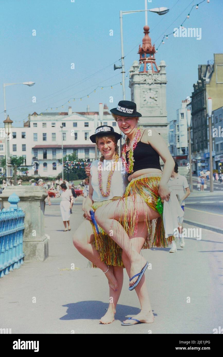 Mujeres jóvenes con vestido de lujo. Sombrero de novedad británico junto al mar, que normalmente lleva las palabras 'Kiss me quick' o 'Kiss me quick, squeeze me slow' Margate, Kent, Inglaterra, Reino Unido. Alrededor de los años 80 Foto de stock