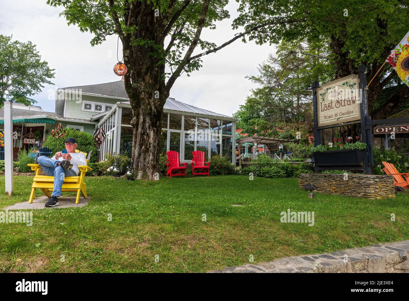 BLOWING ROCK, NC, EE.UU.-20 JUNIO de 2022: La última tienda de paja en la calle principal, muestra el edificio, la señal y un hombre en la silla de lectura de teléfono celular. Foto de stock