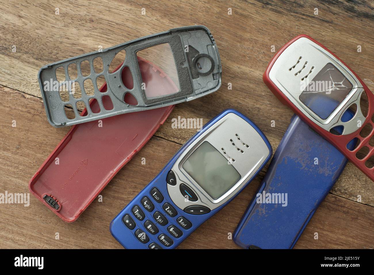 Varios rojo, azul y negro estuches o cubiertas para un botón retro estilo  teléfono móvil o móvil teléfono móvil tendido suelto sobre una mesa de  madera, algunos con grietas y da Fotografía