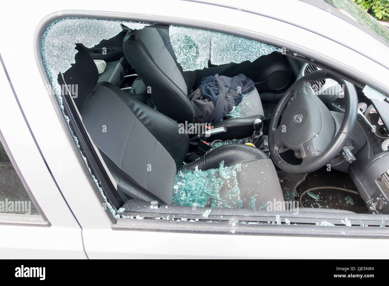 Un coche con la ventanilla lateral del conductor destrozado tras ser atacado por un ladrón. El cristal roto de la ventanilla se muestra en los asientos del interior del vehículo inseguro Foto de stock