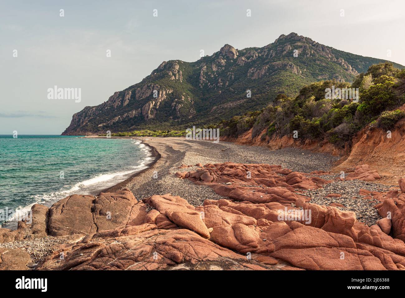 La playa de guijarros gris Cocorocci enmarcada por rocas de pórfido rojo y los bosques alrededor de Monte Cartucceddu en la costa este de Cerdeña, Ogliastra, Italia Foto de stock