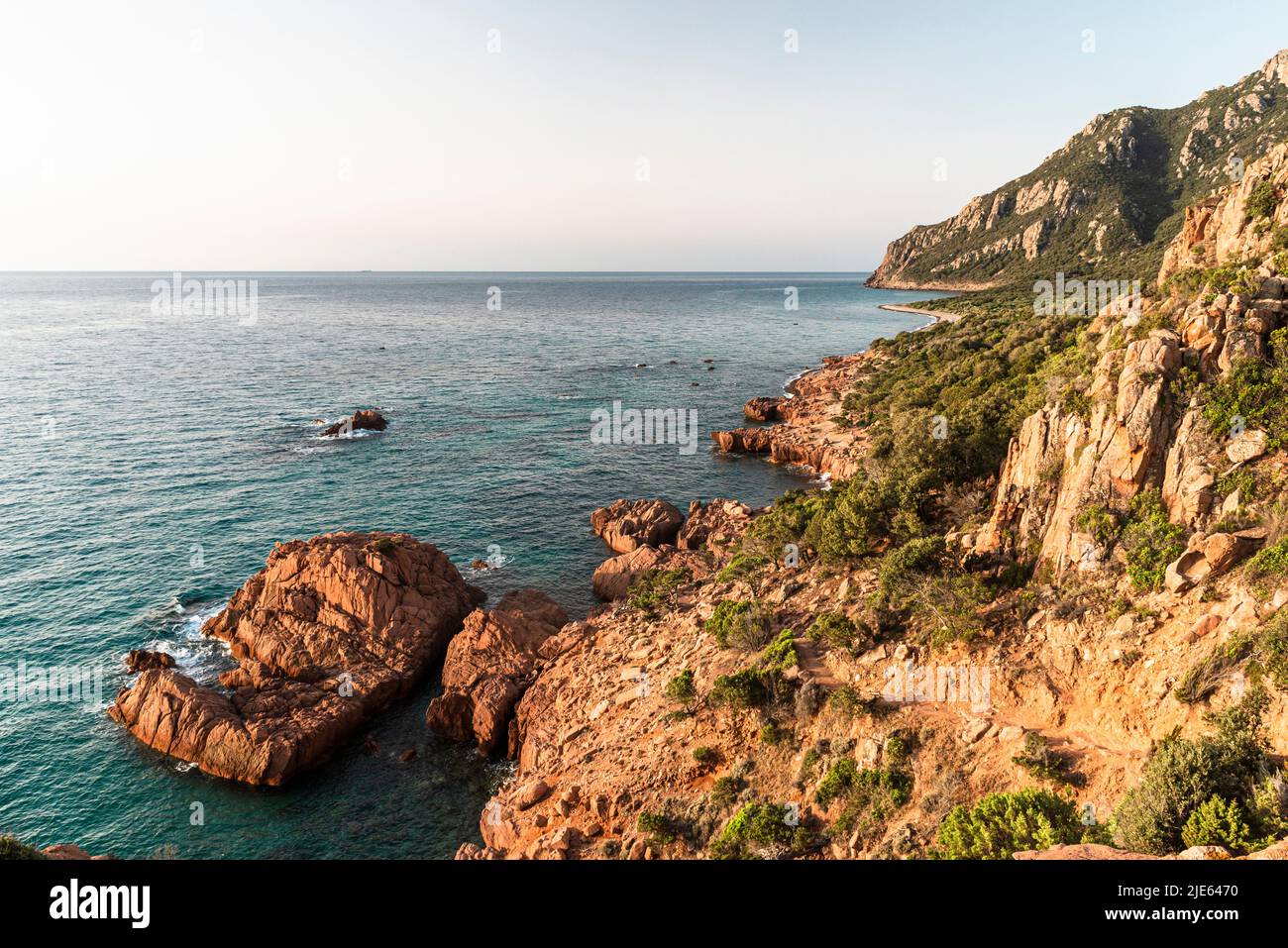 Sol de la mañana en las rocas de pórfido rojas en la bahía de Cocorocci y los bosques alrededor de Monte Cartucceddu en la costa este de Cerdeña, Ogliastra, Italia Foto de stock