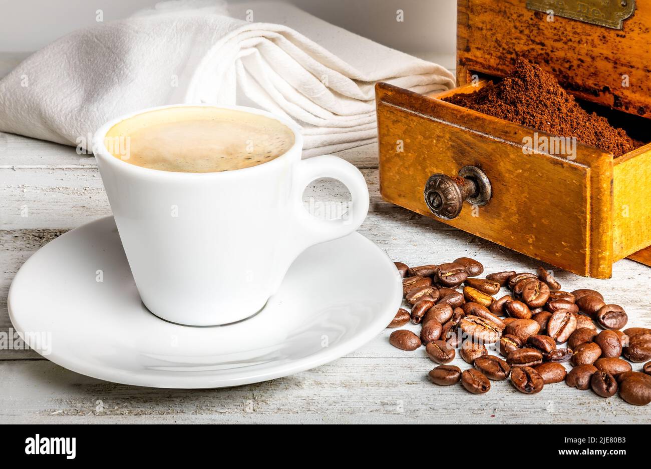 Una taza de café caliente y un viejo molinillo de café sobre una mesa blanca de madera Foto de stock