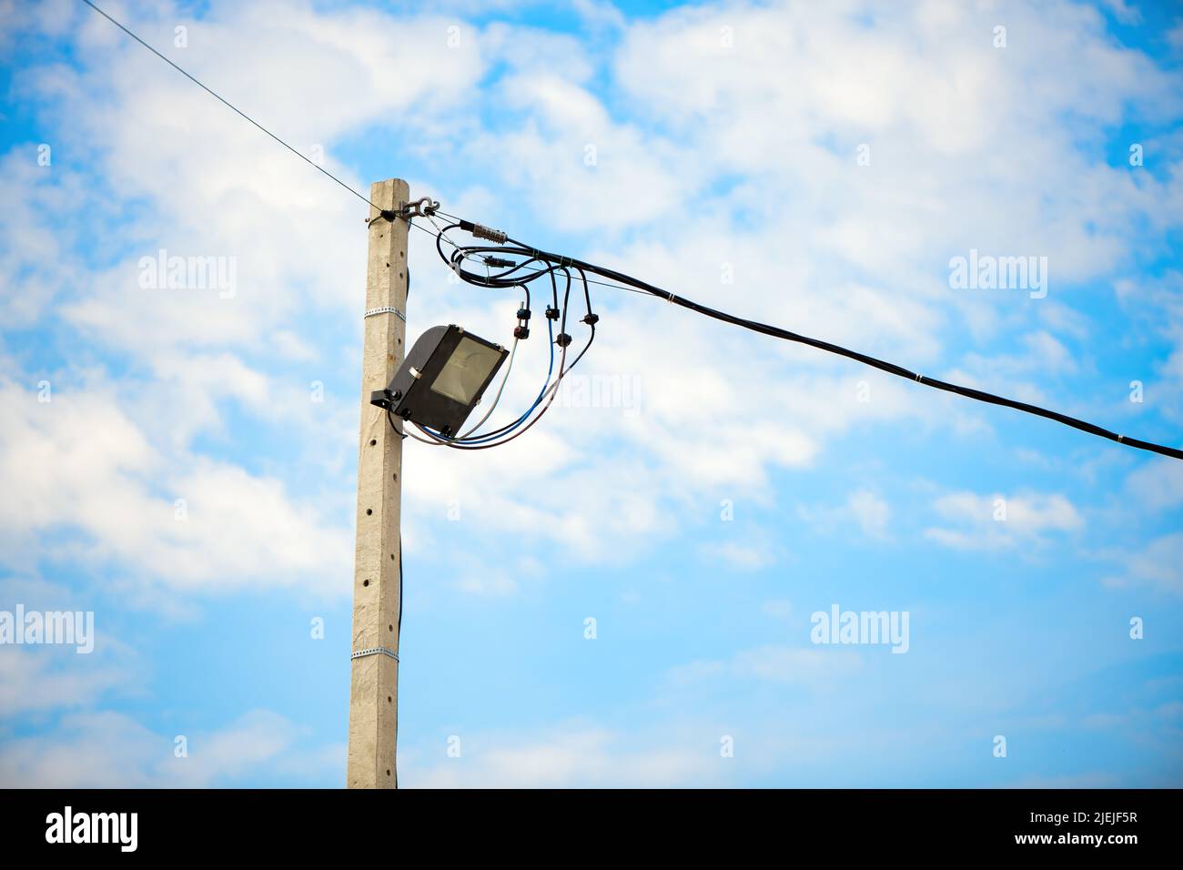 La luz de la calle sobre un poste de hormigón contra el cielo azul y las nubes Foto de stock