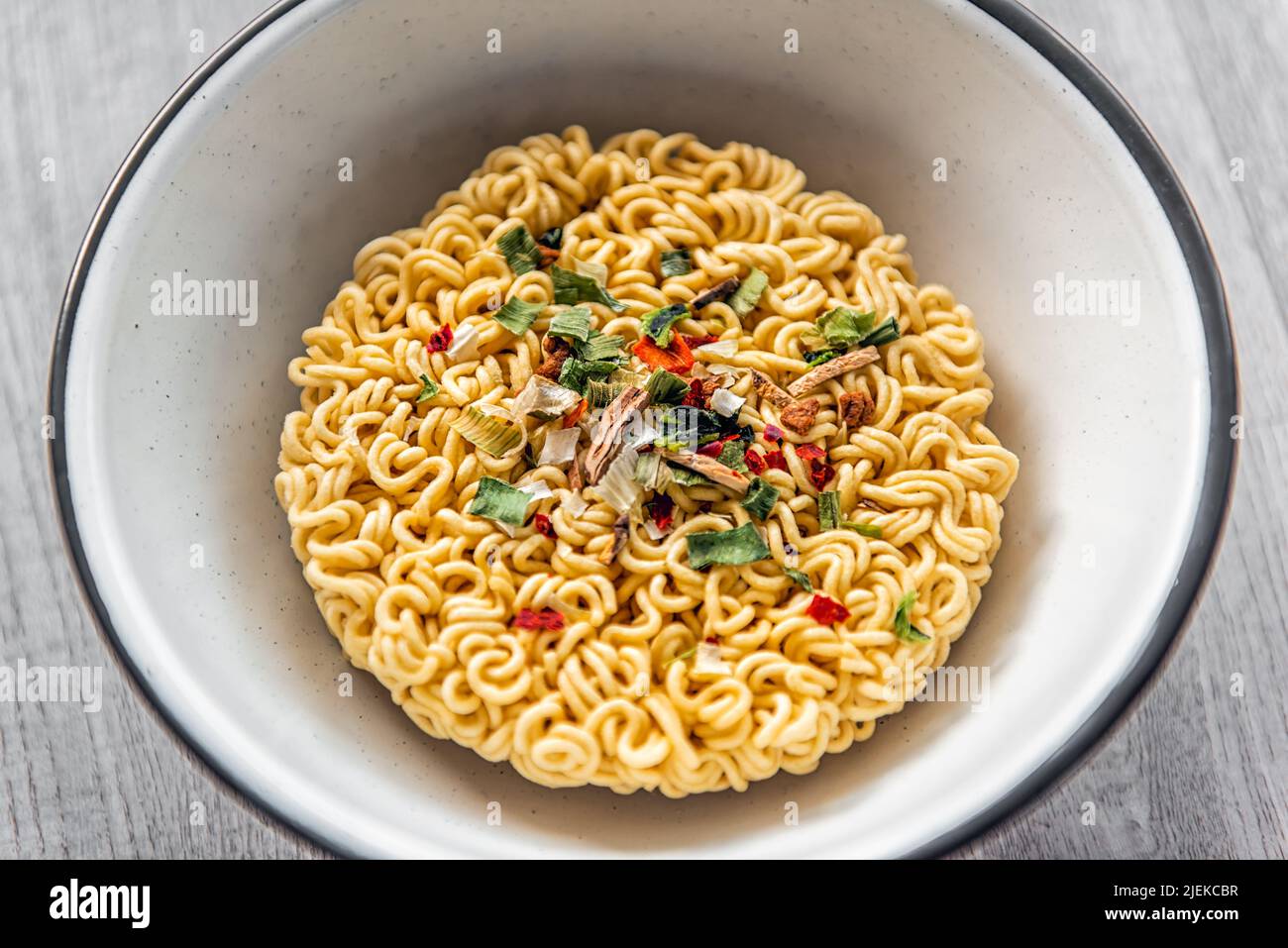Primer plano de sopa instantánea de fideos rojos picantes y secos en un recipiente como comida asiática japonesa con textura de pasta cruda sin cocinar y aderezos de cebolla verde Foto de stock