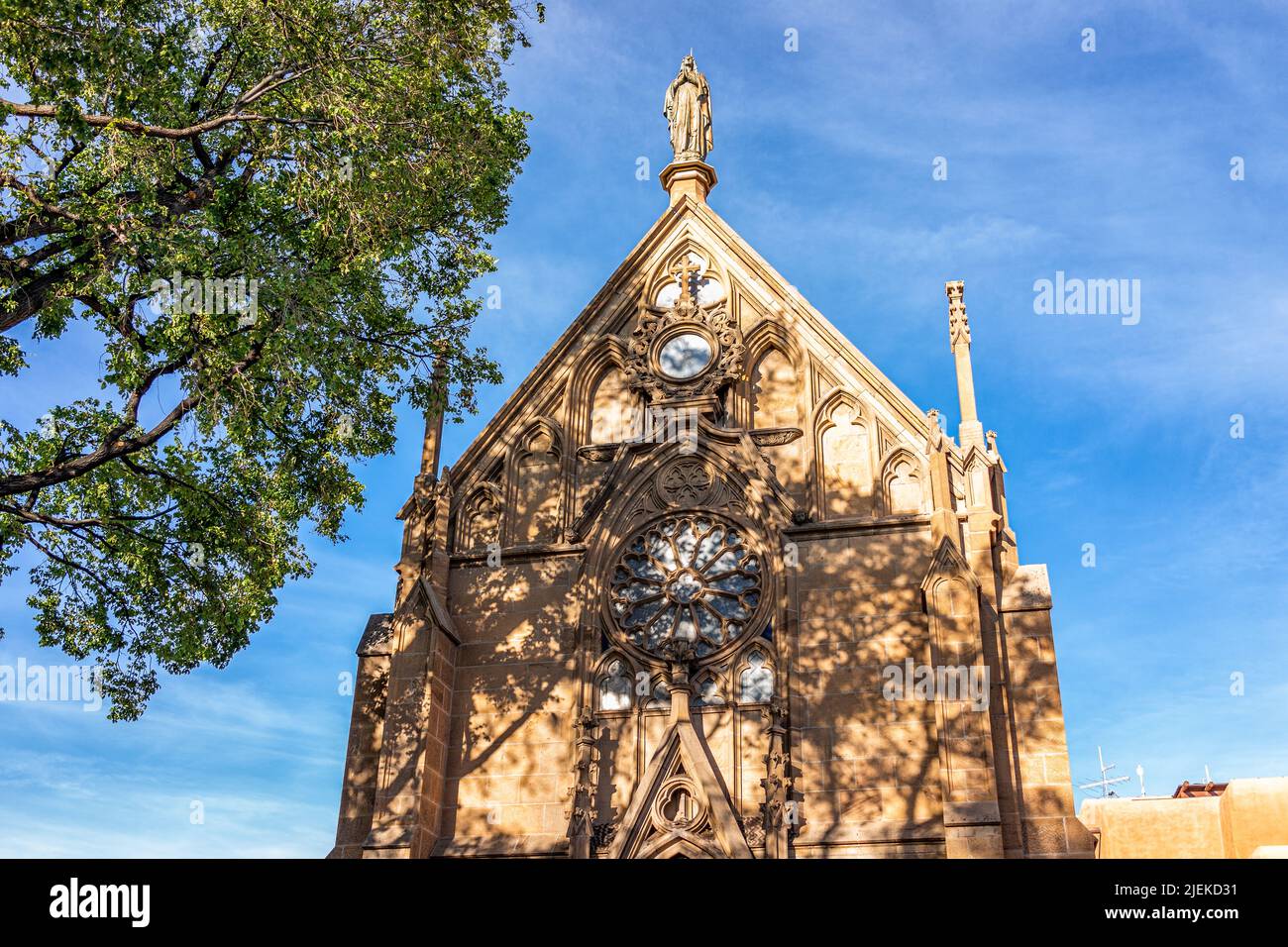 La Capilla Loretto antigua iglesia histórica en Santa Fe, Nuevo México en Estados Unidos con primer plano de fachada exterior y sombra de árboles en un día soleado contra b Foto de stock